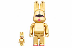 Two glossy gold rabbit-eared figures with pink lips and soles, one small and one large, stand on white.
