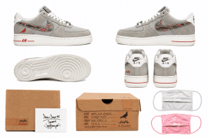 A pair of gray suede Nike Air Force 1 shoes with red accents, boxes, and two face masks.