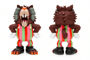 A brown furry monster toy with gray horns, an orange nose, and an open mouth, wearing red, pink, and green striped overalls.