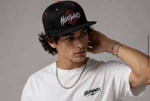 A young man with curly hair wears a black cap with "HEATWAVES" and a white t-shirt.
