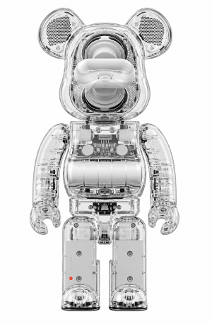 A clear plastic Bearbrick figure reveals internal speakers, circuitry, and batteries against a white background.