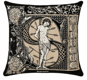 A black and tan cushion features an embroidered St. Sebastian, pierced by arrows, within an ornate "S" and "Supreme" text.