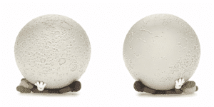 Two textured, light gray moon spheres rest on brown KAWS Companion figures with white gloved hands.