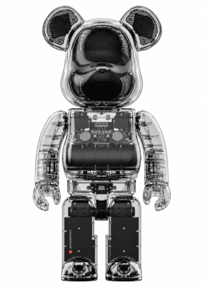 A transparent Bearbrick speaker with visible internal components, black speaker grilles, and a red light on its leg.