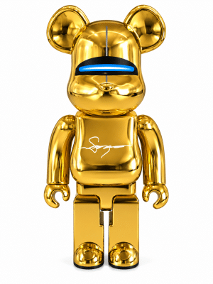 A shiny gold Bearbrick figure with a blue glowing visor and a white signature on its chest.